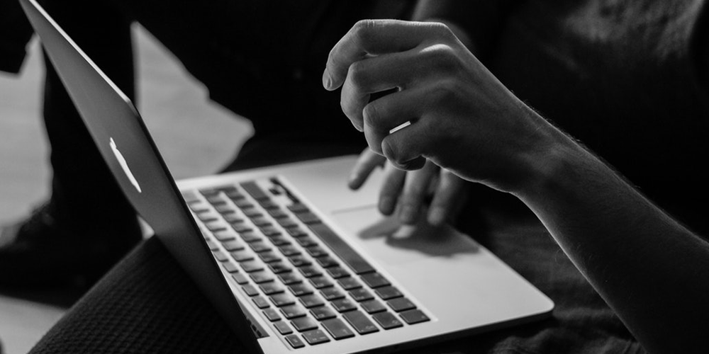 A black and white photo of someone's hands typing on a Mac laptop