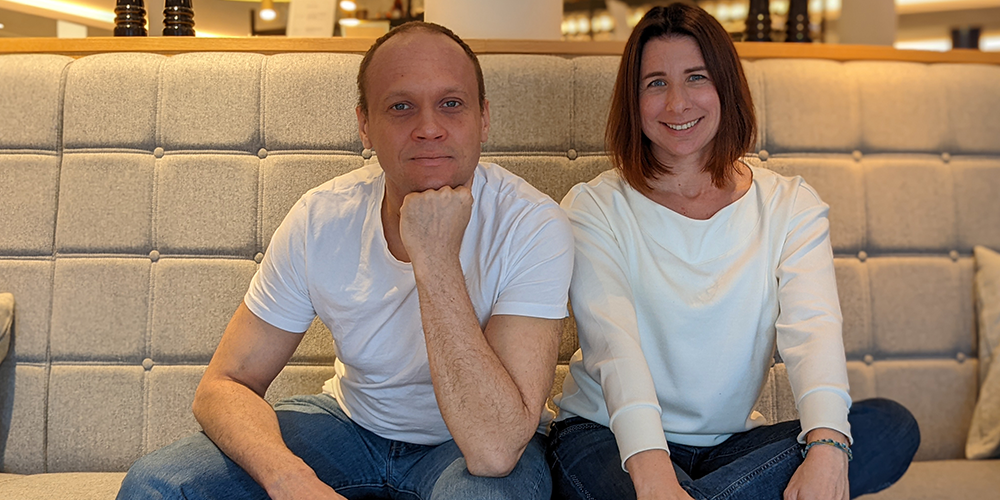 A man and a woman in white shirts and jeans sitting on the couch and posing for a photo