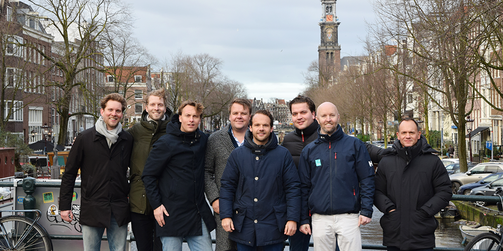 A group of men standing on a bridge in Amsterdam, posing for a photo