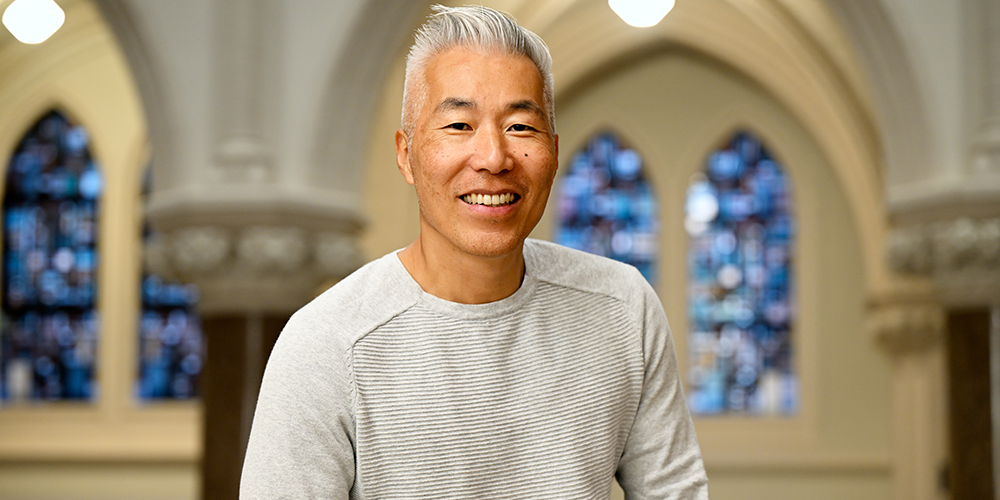 Asian man with grey hair, wearing a grey shirt, posing for a photo