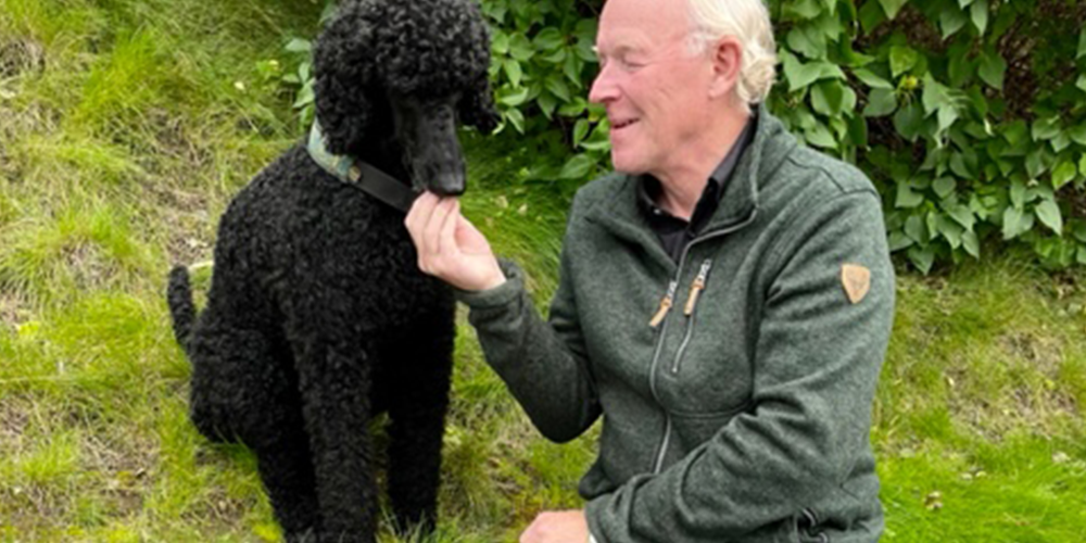 A man wearing a dark green sweatshirt, sitting in a park with his dog