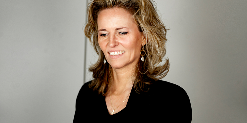 A woman with blonde hair, wearing a black blouse, posing for a photo