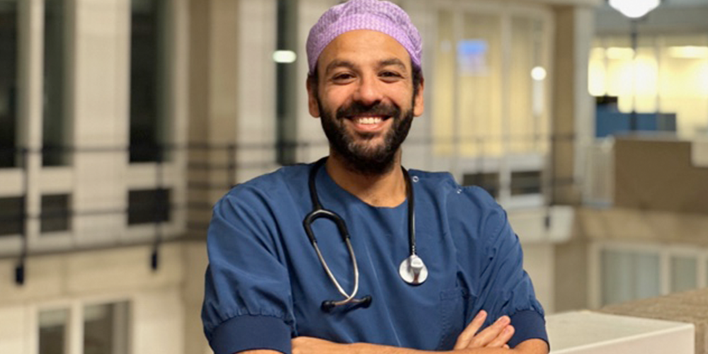 A doctor with a beard, wearing a blue shirt and a stethoscope, posing for a photo